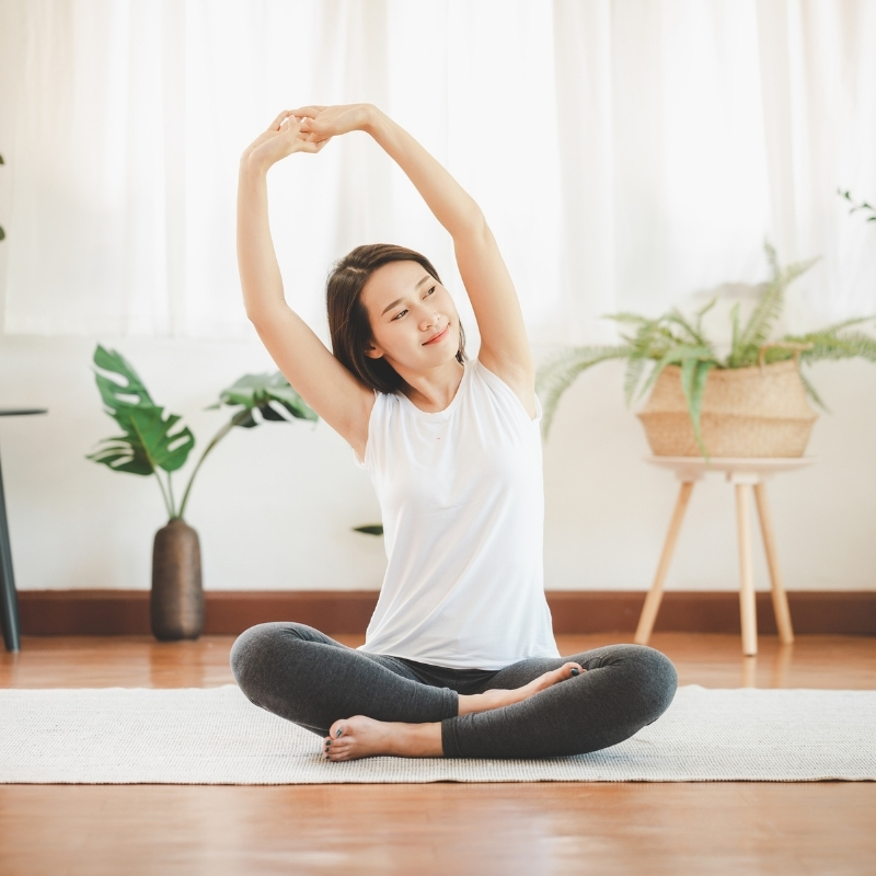 mulher alongando em casa sentada no tapete de yoga