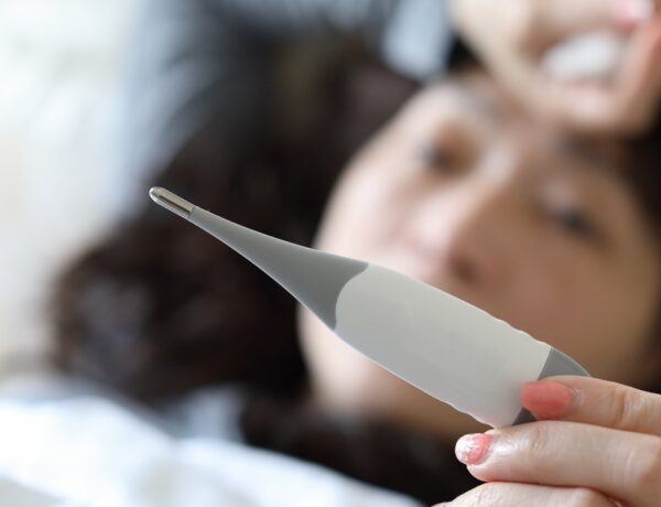 mulher com termômetro na mão esquerda olhando a marcação de temperatura deitada na cama